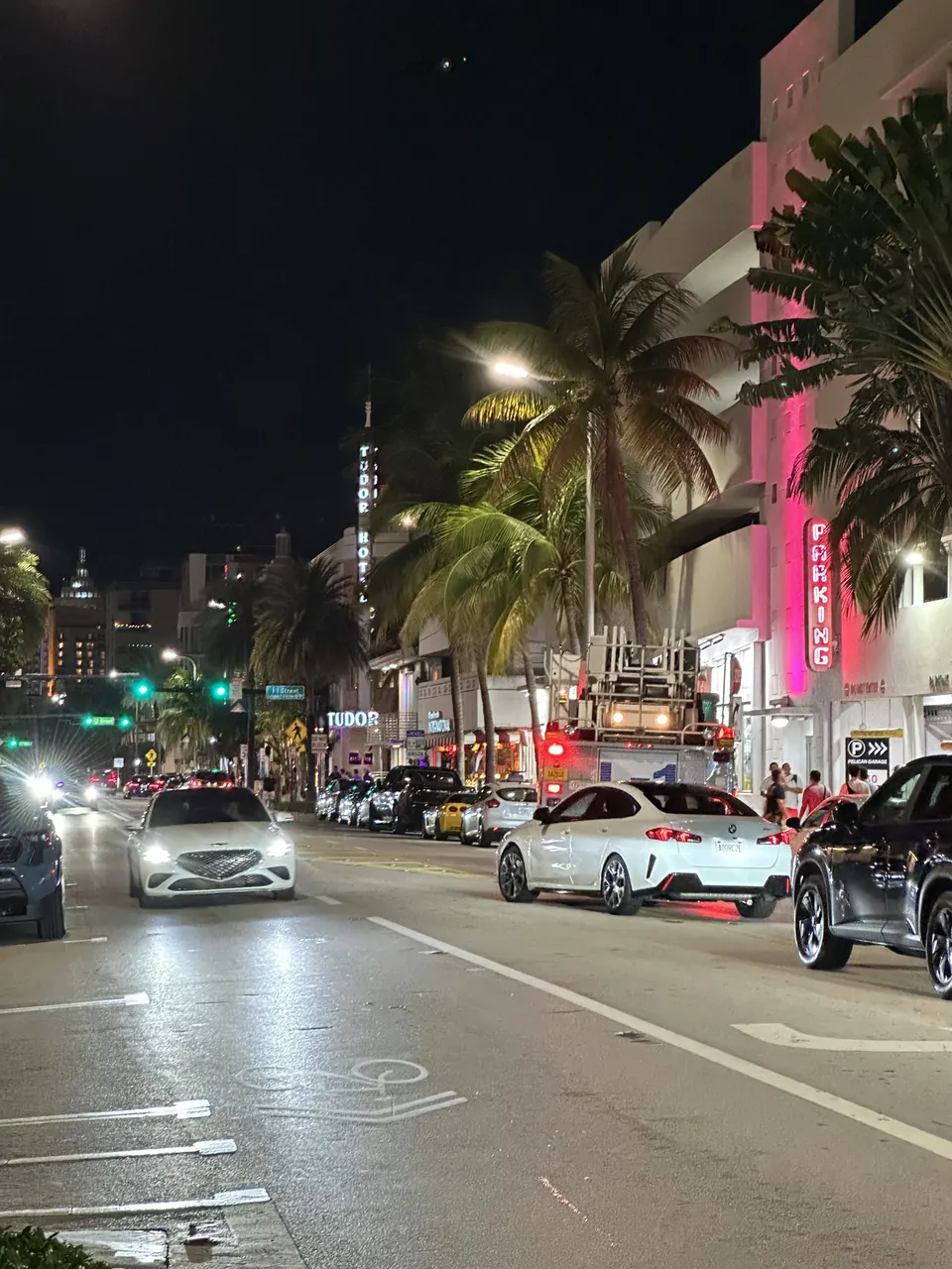 Gece Ocean Drive boyunca aydınlatılan binalar, palmiyeler ve araçlar.