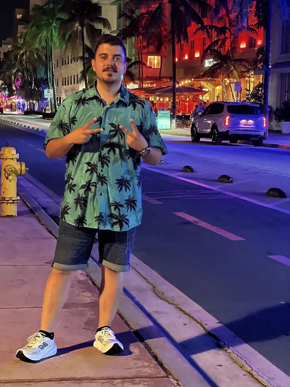 Gece Miami’de, renkli ışıkların önünde kameramla duruyorum.