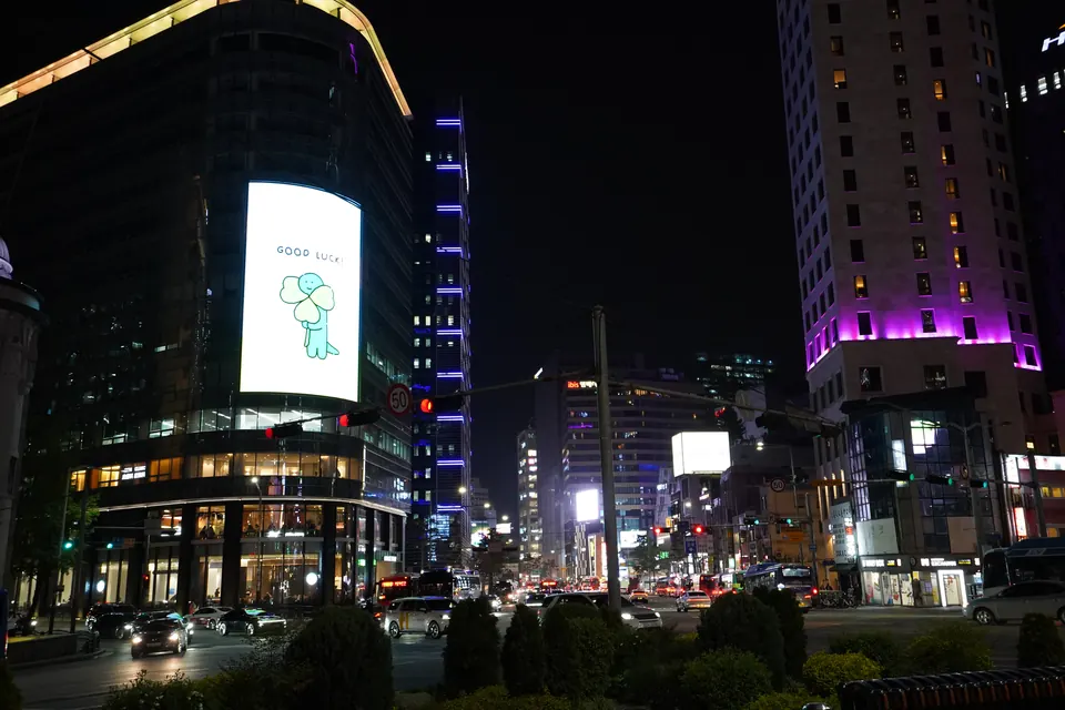 Dijital ekranlar, mor ışıklı bina ve Seul’de gece trafiği.
